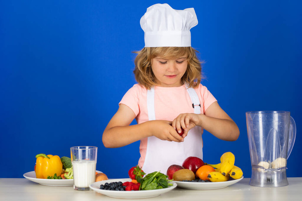 Child chef dressed cook baker apron and chef hat isolated on studio background. Healthy nutrition kids food - Zdjęcie, obraz