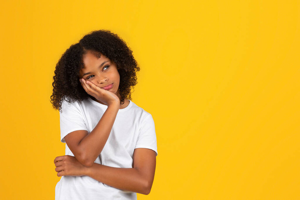 Sad pensive tired adolescent curly girl in white t-shirt looks at empty space, think, isolated yellow studio background. Stress, problems at study, knowledge in school, pupil emotions - Fotoğraf, Görsel