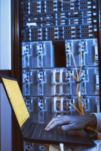 Lets diagnose and fix this quickly. Closeup shot of an unrecognisable man using a laptop while working in a server room - Foto, Imagen