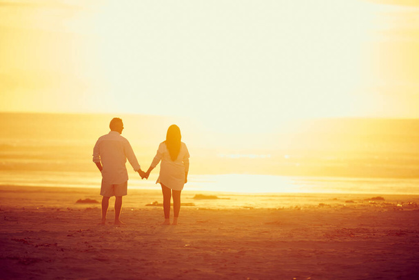 Gemeinsam im Paradies. Rückansicht eines liebevollen reifen Paares, das Hand in Hand am Strand spaziert - Foto, Bild