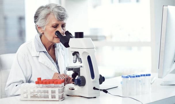 Après tant d'années, je suis toujours surpris dans cette carrière. une scientifique âgée concentrée regardant à travers un microscope alors qu'elle était assise dans un laboratoire - Photo, image