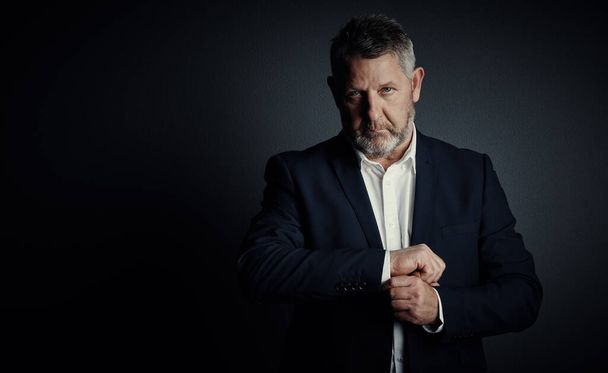 Its time to suit up. Studio portrait of a handsome mature businessman buttoning his sleeves while standing against a dark background - Фото, изображение
