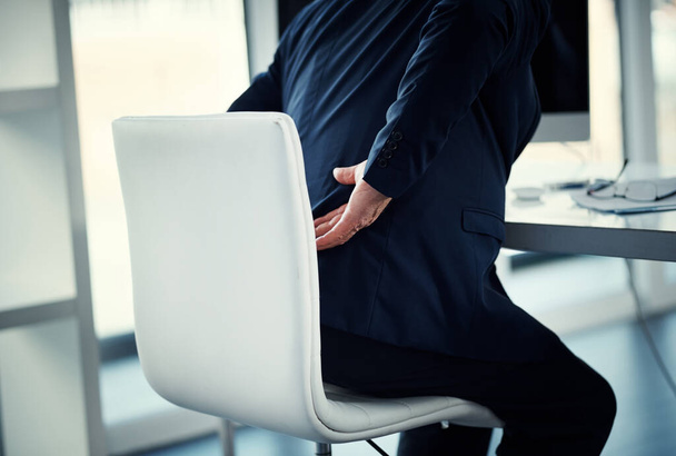 His back is carrying his workload. a businessman experiencing back ache while working at his desk - Photo, image