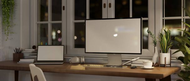 Comfortable and minimalist home workspace at night with PC computer and laptop mockup, stationery and decor on a wooden table against the window. 3d render, 3d illustration - Fotoğraf, Görsel