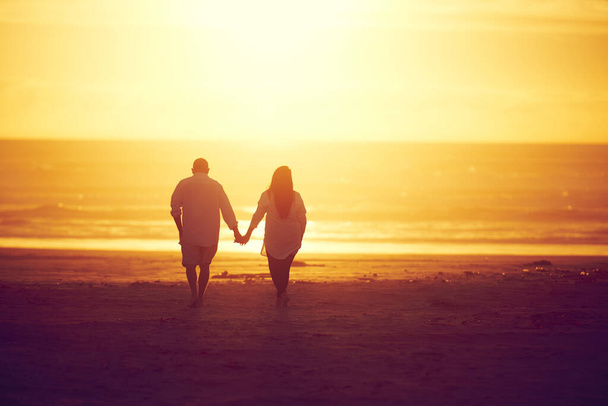 Вместе сквозь закаты и восходы солнца. Снимок ласковой зрелой пары, идущей рука об руку на пляже - Фото, изображение