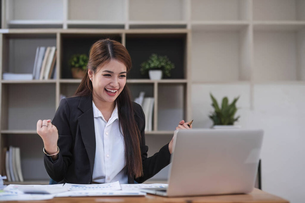 Beautiful Asian businesswoman celebrate while using laptop at office and showing delight. Startup small business and successful concept... - Foto, Imagen