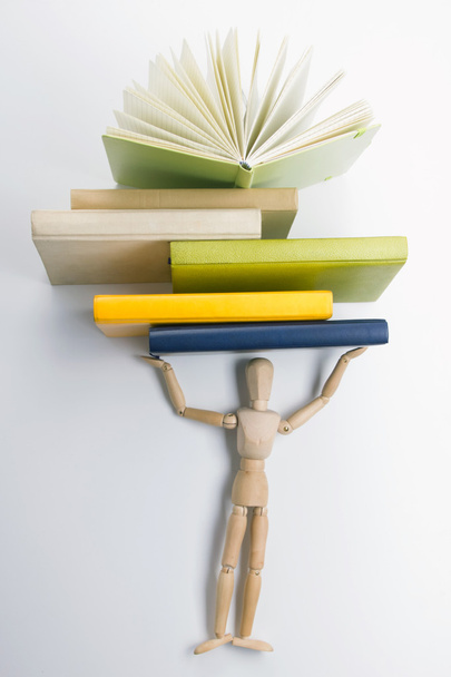 Drewniany manekin prowadzi stos kolorowych książek. - Zdjęcie, obraz