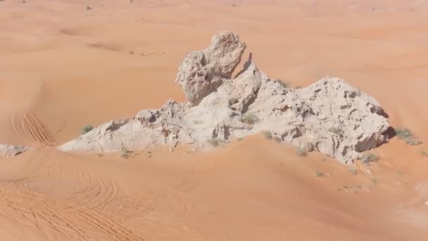 Um drone voa em torno de um homem barbudo vestido como um xamã que ora em um penhasco no deserto arenoso dos Emirados Árabes Unidos. Vista aérea - Filmagem, Vídeo