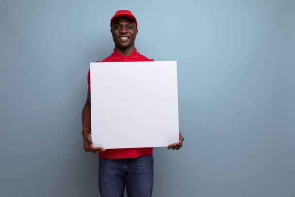 jong levering werknemer amerikaanse man in rood t-shirt en honkbal pet houden papier mockup. - Foto, afbeelding