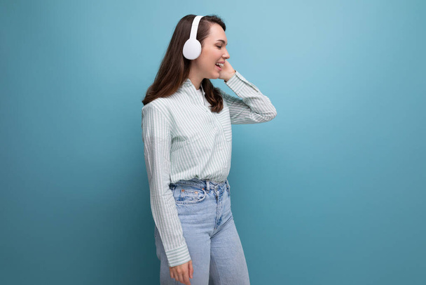 20s brunette lady in shirt and jeans listening to playlist in wireless headphones. - 写真・画像