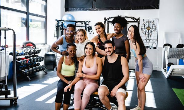 Fiatal, multiracionális nők és aktív ruhás férfiak csoportja boldogan mosolyog, miközben összegyűlnek a kortárs edzőteremben - Fotó, kép