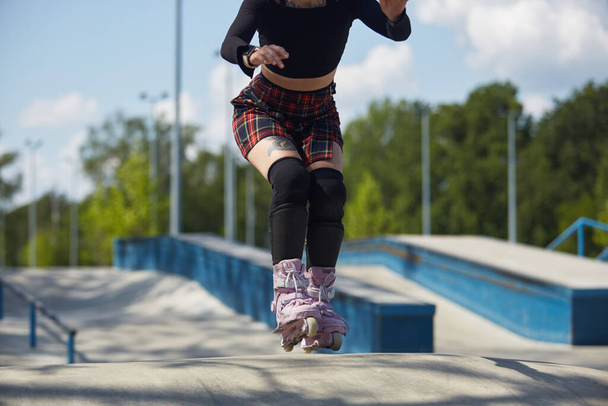 Young skater girl riding in a skatepark. Aggressive inline roller blader female skating in a outdoor concrete park - Фото, зображення