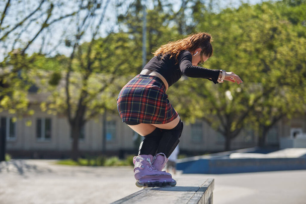Young skater grinding on a ledge in a skatepark. Cool female roller blader in aggressive inline skates performing a ao pornstar trick  - Foto, Bild