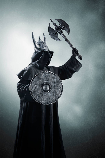 Warrior with horned helmet, double headed battle axe and round shield in the dark - Φωτογραφία, εικόνα