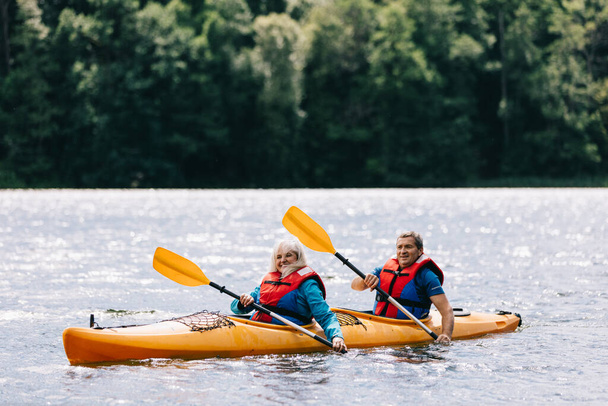 Happy senior active couple kayaking on lake enjoying time together - Photo, Image