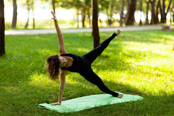Woman practices yoga in morning in park in fresh air. Side Plank pose. - Foto, afbeelding