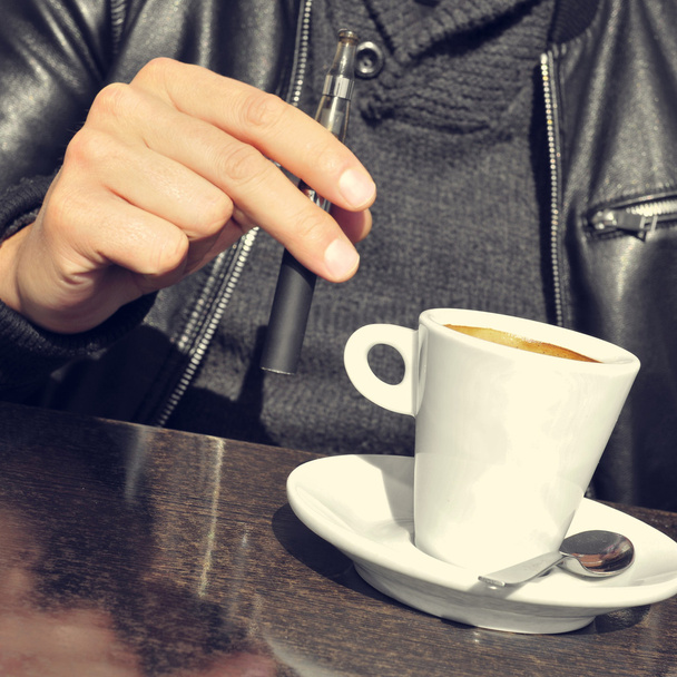 junger Mann mit elektronischer Zigarette und einer Tasse Kaffee in der Hand - Foto, Bild