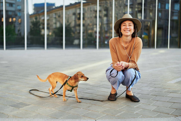 Joven mujer adulta en la ciudad con un perro sentado y abrazando, sonriendo. Mascotas del perro, alimentación, divertirse Foto de alta calidad - Foto, Imagen