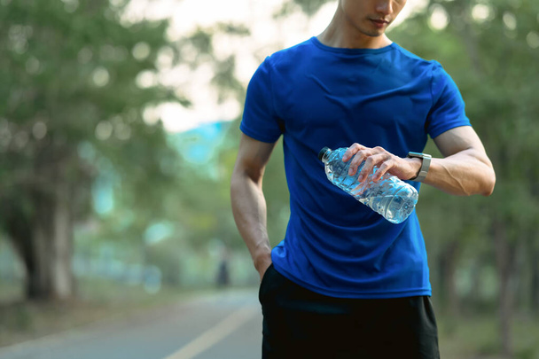 Erkek sporcu elinde bir şişe su tutuyor ve antrenman sonuçlarını izlemek için akıllı adımları kontrol ediyor. Sağlıklı yaşam tarzı, sağlık konsepti. - Fotoğraf, Görsel