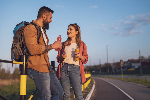 Couple heureux reposant à côté de la route et buvant du jus de rafraîchissement. - Photo, image