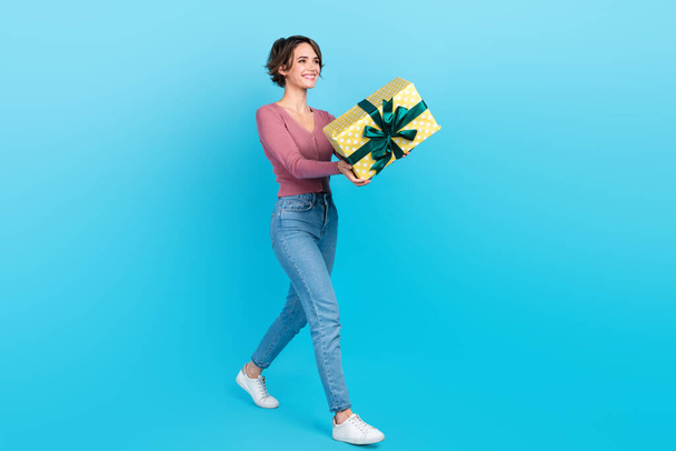 Full length profile photo of pretty positive person arms hold giftbox give empty space isolated on blue color background. - Foto, Imagen