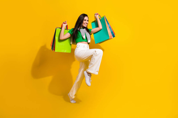 Full length photo of excited funky girl dressed green t-shirt rising bargains running empty space isolated yellow color background. - Fotografie, Obrázek