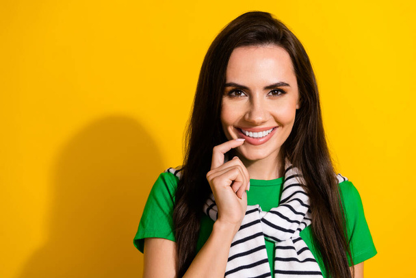 Photo of charming tricky girl dressed green t-shirt finger chin smiling empty space isolated yellow color background. - 写真・画像