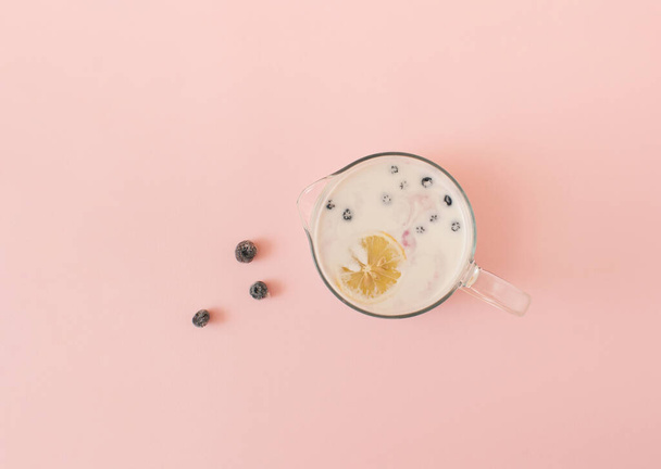 Creative layout made of iced blueberries with a jug of milk isolated on pink background.  Top vew. Minimal summer exotic concept with copy space. Flat lay. - 写真・画像
