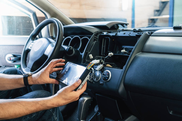Auto in Car Service, proces van het installeren van moderne 2-din radio geluidssysteem. Auto elektrische handen op dashboard vaststelling probleem close-up. - Foto, afbeelding