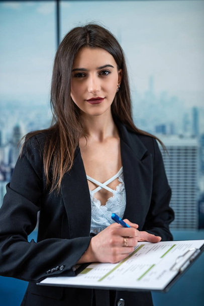 Eine einzige glückliche selbstbewusste kaukasische Managerin im Anzug, die im Büro mit Dokumenten posiert. Erfolgreiche Geschäftsfrau - Foto, Bild