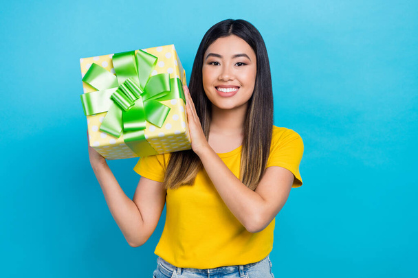 Photo of young chinese girl wear yellow t-shirt hold box package holidays party event receive present isolated on blue color background. - 写真・画像