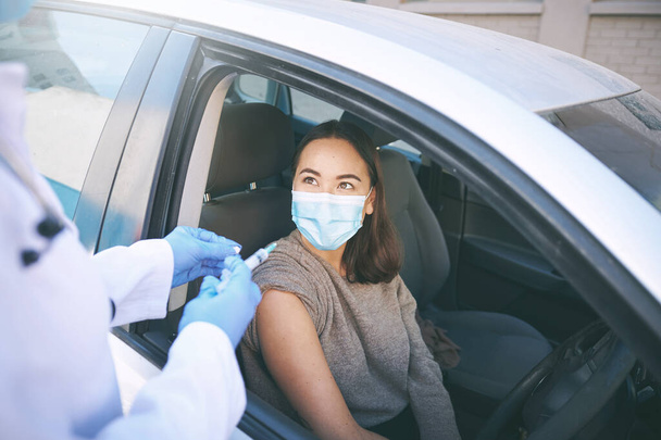 Every vaccination campaign contributes towards a safer community. a masked young woman receiving an injection at a Covid-19 drive through testing centre - Photo, Image