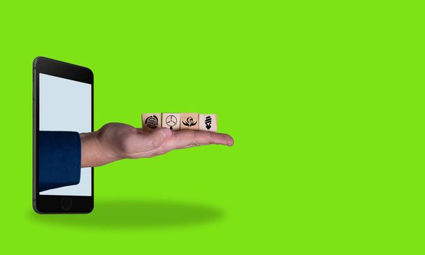 Цифровой художественный коллаж, рука с деревянными кубиками, выходящими из телефона на зеленом фоне. Экологические продукты. Концепция использования чистых систем. - Фото, изображение