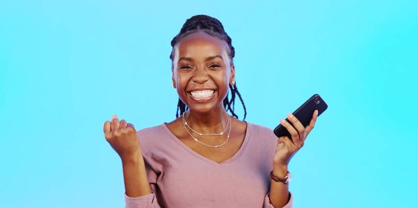Wow, happy and excited black woman with phone receiving email news of bonus, promotion or announcement in studio. Winning, prize notification and African girl celebrating with smile on blue backgrou. - Valokuva, kuva