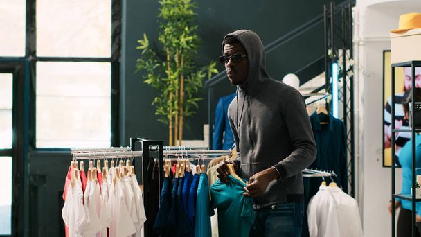African american robber stealing trendy clothes in modern boutique, being caught by asian security guard. Thief running from bodyguard, trying to escape the accusations. Crime concept - Valokuva, kuva