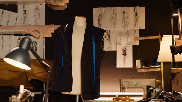Manekin krawiecki i szkice w pracowni mody, narzędzia używane do produkcji linii ubrań na zamówienie. Manekin figuralny z tkaniną, taśmą pomiarową i przedmiotami do szycia. - Zdjęcie, obraz