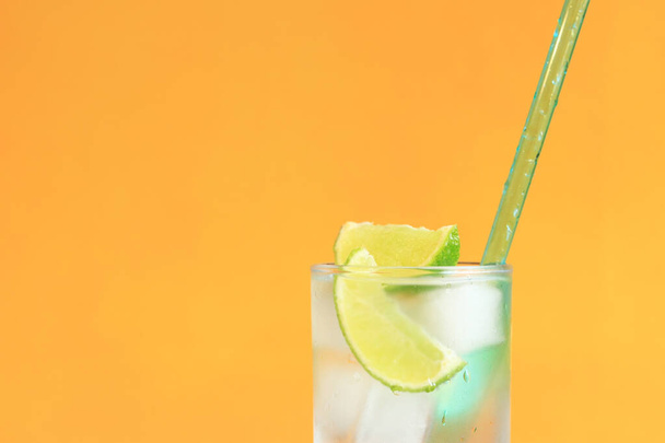 Lemonade with ice and lime on a bright orange background. Summer cocktail with cold drink. Copy space. Drink with a straw close-up - 写真・画像