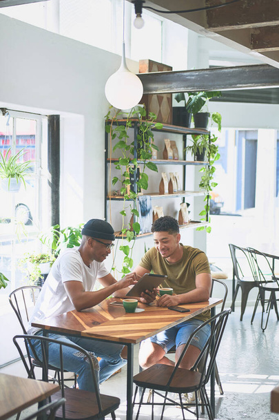 Spójrz na to. dwóch przystojnych przyjaciół siedzących razem i łączących się przy kawie w kawiarni w ciągu dnia - Zdjęcie, obraz