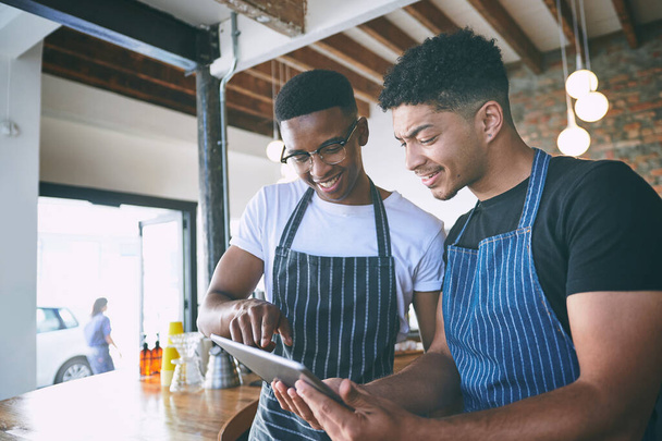 Eingängiges digitales Marketing hält die Türen offen. zwei junge Männer, die während ihrer Arbeit in einem Café ein digitales Tablet benutzen - Foto, Bild