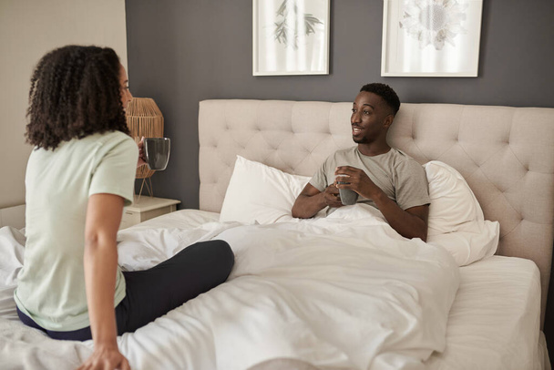 Young multiracial couple smiling and talking together on their bed over cups of coffee in the morning - Fotoğraf, Görsel
