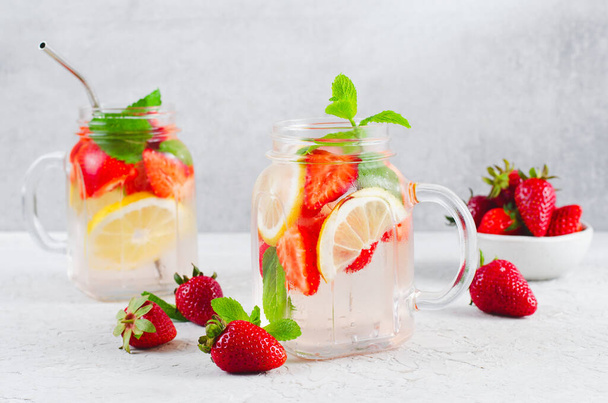 Βραστό νερό φράουλας, δροσιστικό κοκτέιλ, λεμονάδα, αποτοξίνωση, καλοκαιρινό παγωμένο ποτό με φρέσκια φράουλα, λεμόνι και μέντα σε φωτεινό φόντο - Φωτογραφία, εικόνα