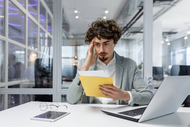Sad and upset mature businessman received an envelope by mail with a bad news notification letter, boss in business suit working inside office using laptop wearing glasses and beard. - Foto, Bild