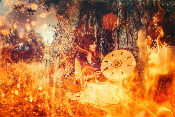 krásná šamanská dívka hraje na šaman rám buben v přírodě. Požární pozadí - Fotografie, Obrázek