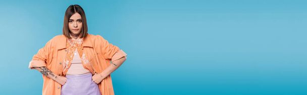 offended woman standing with hands on hips on blue background, looking at camera, emotional, displeased, generation z, short brunette hair, pierced nose, tattooed, banner  - Foto, Imagem