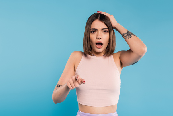 shocked face, brunette young woman with short hair, tattoos and nose piercing pointing at camera on blue background, generation z, displeased, casual attire, summer outfit  - Photo, Image
