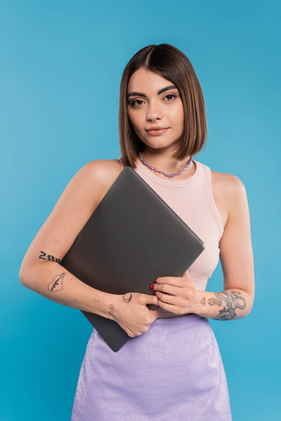 freelancer, brunette young woman with short hair, tattoos and nose piercing holding laptop on blue background, generation z, summer trends, attractive, remote work, everyday style  - Photo, Image