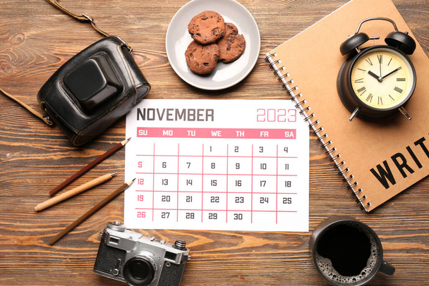 Composition with calendar, photo camera, cup of coffee and cookies on wooden background - 写真・画像