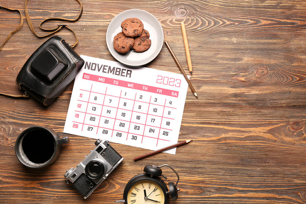 Composition with calendar, photo camera, cup of coffee and cookies on wooden background - Photo, Image