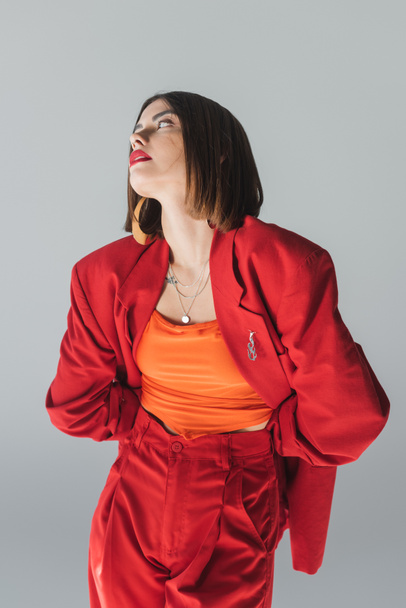 Dame in Rot, junge brünette Frau mit kurzen Haaren posiert im Anzug auf grauem Hintergrund, Generation Z, trendiges Outfit, modisches Modell, professionelle Kleidung, Führungsstil  - Foto, Bild