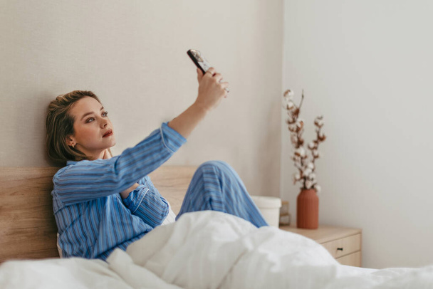 Young happy woman taking selfie in a bed. - Foto, afbeelding